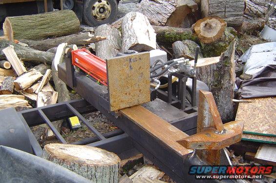 Hydraulic log splitter with orange cylinder, surrounded by cut logs