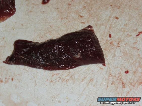 Raw meat slice on a cutting board with red smudges and a Supermotors.net watermark