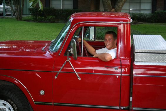 Young man in driver's seat of red pickup truck with toolbox in bed