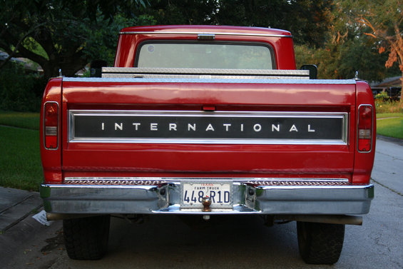 Red pickup truck rear with 'INTERNATIONAL' tailgate badge and Texas Farm Truck license plate