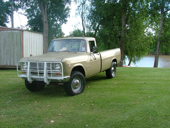 1975 International pickup truck with a white grille guard parked on grass near trees and water