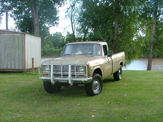 Tan 1975 International pickup truck with a chrome grille guard parked on grass near a body of water