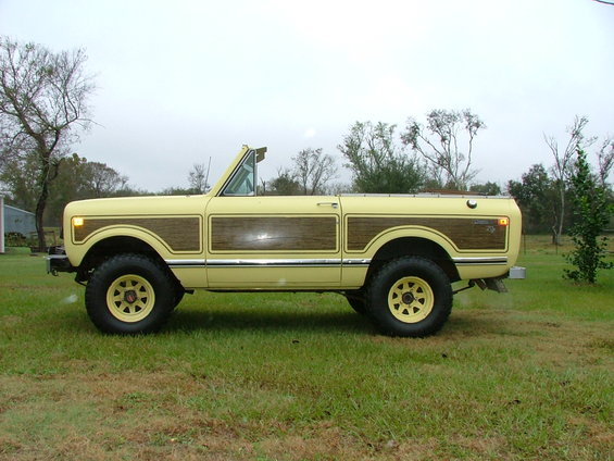 Yellow 1975 International Scout II with wood paneling, side view, parked on grass
