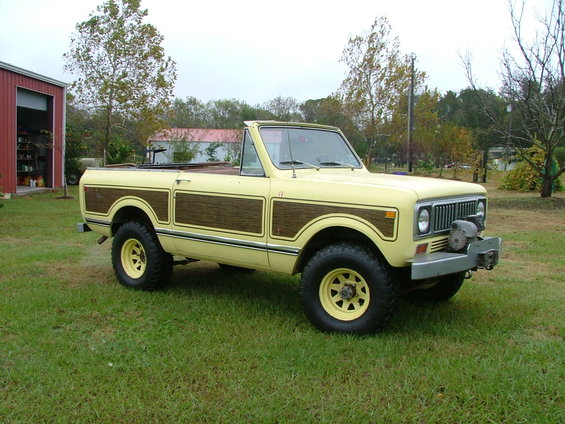 Yellow convertible SUV with wood paneling, parked on grass near a red barn