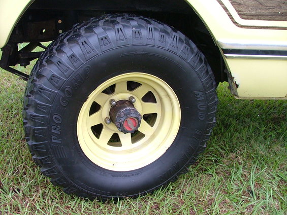 Yellow-painted wheel with "Pro Comp Mud" tire on a light-colored vehicle with wood paneling