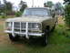 1975 International Scout II - A tan 1975 International pickup truck with a prominent white grille guard is parked on a grassy lawn.