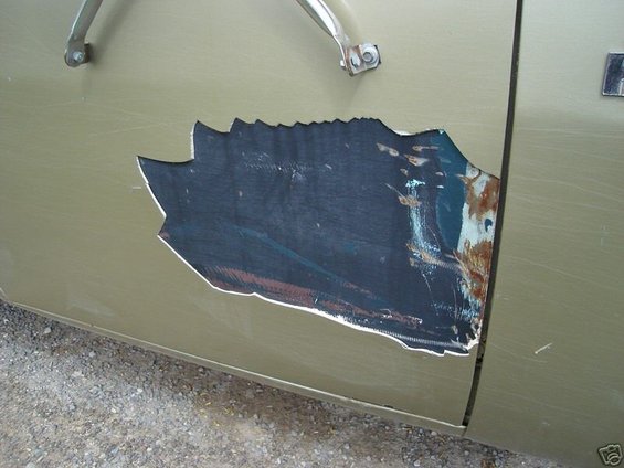 Close-up of a damaged vehicle door with a large hole showing rust and underlying material