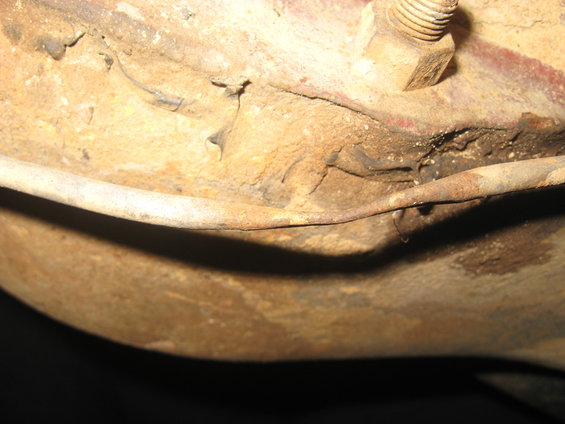 Close-up of rusted metal frame with a bolt and wire, showing significant corrosion