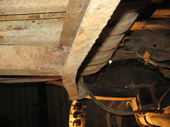 Underside of a rusty vehicle showing frame, fuel tank, and tire