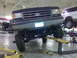 1990 Ford Bronco - A modified Ford Bronco is raised on a hydraulic lift in a garage, showing its custom suspension.