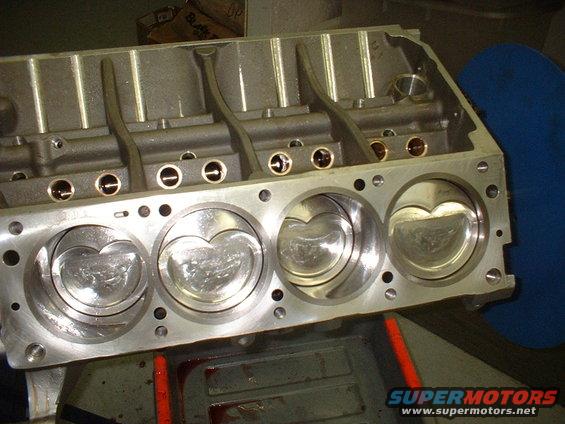 Engine block with four pistons visible, showing cylinder bores and valve train components