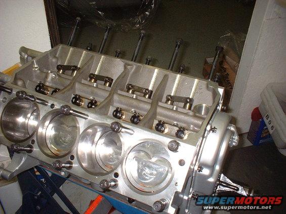 Aluminum engine block with four cylinders visible, showing pistons and valve train components