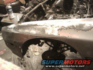 Car fender being repaired, showing primer and bodywork. A can of spray paint is on a workbench