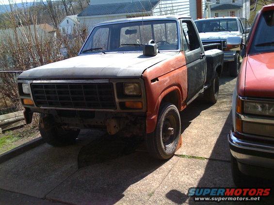 Ford F-150 pickup truck, primer red and dark gray, front driver side view, parked on concrete