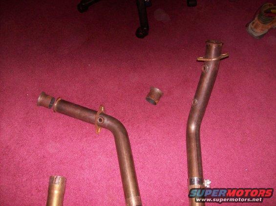 Close-up of three bent metal exhaust pipes against a red background
