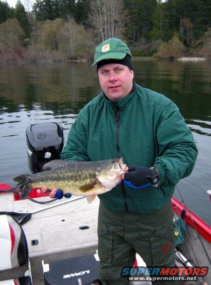 Man holding a large bass on a boat with a boat motor in the background