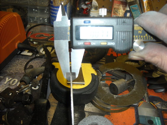 Digital calipers measuring a small metal part on a workbench with tools and parts in the background