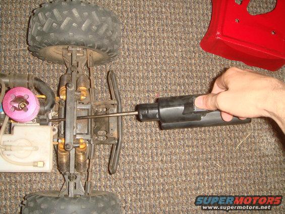 Remote control car chassis with a pink engine, gold shocks, and a hand holding a black tool