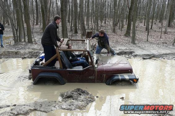 Jeep stuck in mud pit with people trying to push it out