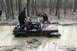 1995 Ford Bronco - A maroon Jeep is submerged in a muddy forest clearing, with several people attempting to free it.