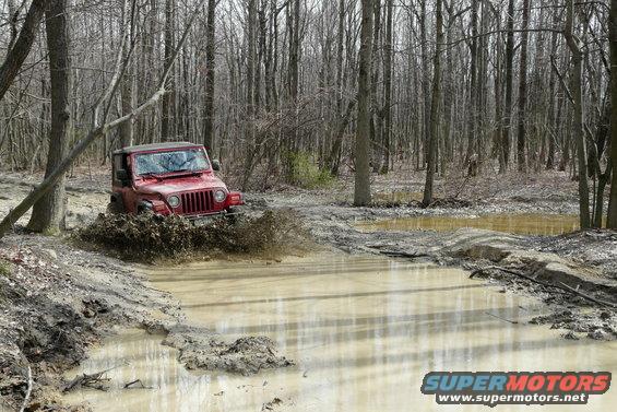 Red Jeep Wrangler splashing through a muddy trail in a forest