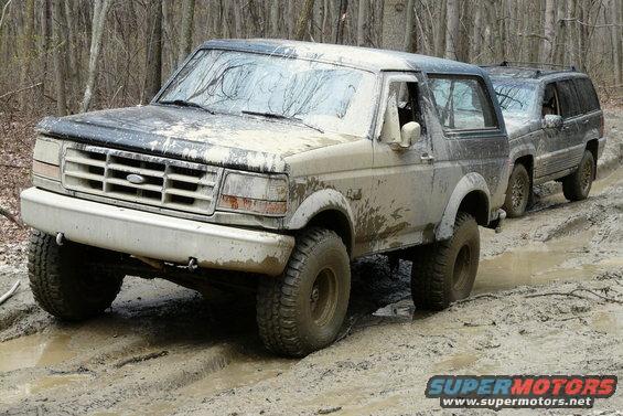 1995 Ford Bronco driving through mud with a Jeep Grand Cherokee behind it