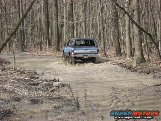 Blue SUV driving through a muddy trail in a forest
