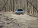 1991 Ford Bronco - A blue SUV navigates a muddy path surrounded by trees.