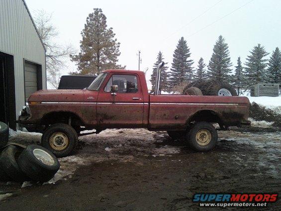 1978 Ford F-150 pickup truck, red, lifted, with large exhaust pipe, parked in muddy yard