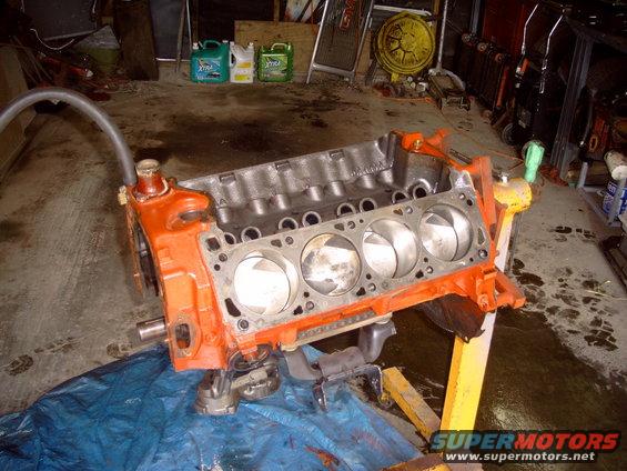 Orange V8 engine block on a yellow stand in a garage