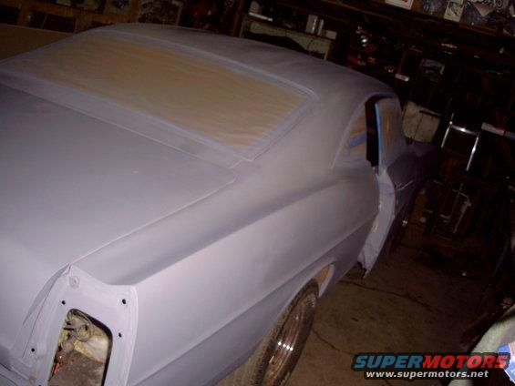 car body with primer on it, windows taped off, in a garage