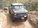 1989 Ford Bronco - A modified black pickup truck tackles a challenging off-road course, with another vehicle visible in the background.