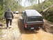 1989 Ford Bronco - A black Ford Bronco navigates a muddy path on a forest trail, with other vehicles visible ahead.