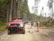 1989 Ford Bronco - Several off-road vehicles line a dirt path through a forest with people standing around.