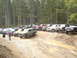 1989 Ford Bronco - Multiple SUVs and trucks are parked on a dirt track in a wooded area, with a muddy puddle in the foreground.