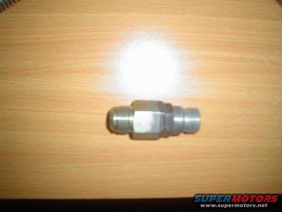 Metal fitting with hexagonal body and threaded ends on a wooden surface