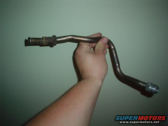 Metal pipe part held by a hand against a green wall