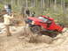 1989 Ford Bronco - A red off-road vehicle navigates a challenging obstacle on a wooded trail with spectators observing.