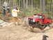 1989 Ford Bronco - A modified red truck tackles a challenging off-road course with onlookers.