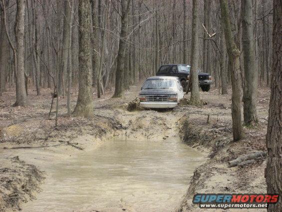 1991 Ford Bronco and another truck navigating a muddy trail in a wooded area