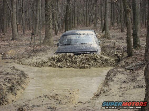 1991 Ford Bronco driving through mud in a forest