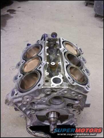 V8 engine block with pistons visible in cylinders. Supermotors.net logo at bottom