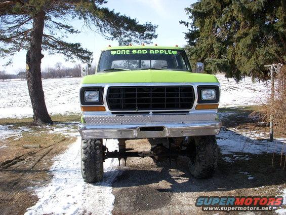 Front view of a lifted, lime green pickup truck with a black grille and chrome bumper. Decal on windshield reads 'ONE BAD APPLE'
