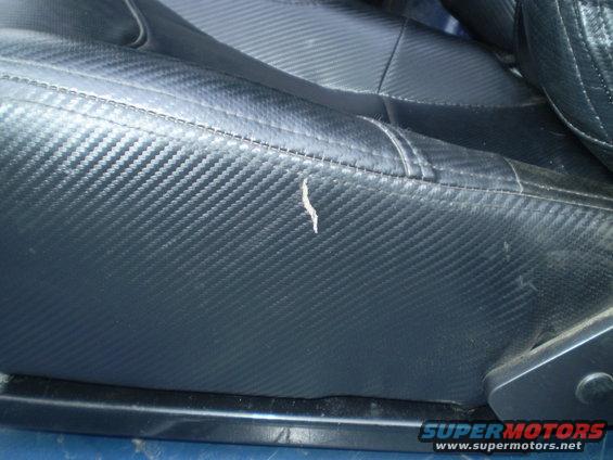 Close-up of a black car seat with carbon fiber pattern and a small tear on the side