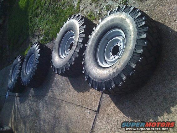 Four off-road tires with aggressive tread patterns and silver rims on a concrete surface
