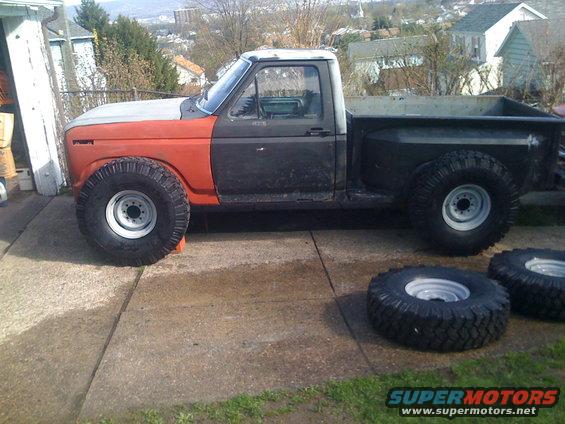 Side view of a 1985 Ford F-150 with large off-road tires and a two-tone paint scheme