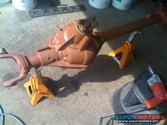Brown Dana 60 front axle assembly on jack stands with a drill and bucket nearby