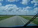 2009 Kenworth T800 - View from a vehicle driving on a highway under a cloudy blue sky.