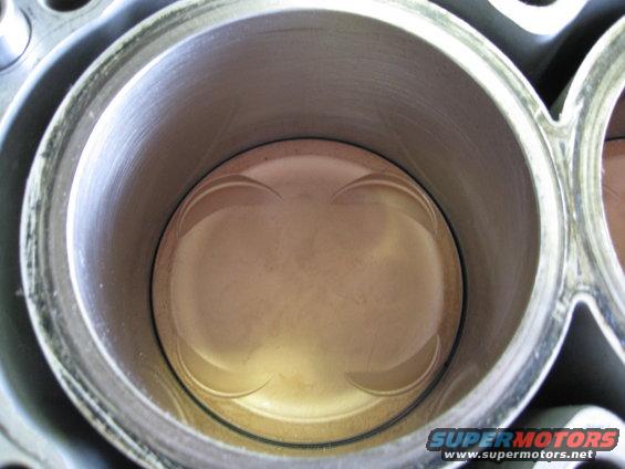 Engine cylinder with piston visible inside, showing wear marks and a metallic sheen