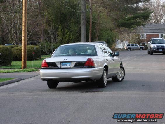 Silver 2003 Ford Crown Victoria sedan driving away, license plate B89-UTA. Another SUV is visible in the background